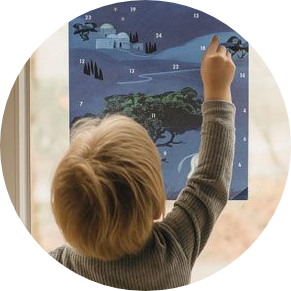 Kind zeigt auf den Fensterbild-Adventskalender am Fenster